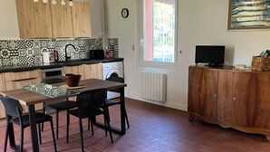 A kitchen with a dining table, chairs, a washing machine, a radiator, and a TV. - Le Refuge de Crèvecœur (Clef Vallée d'Eure)