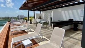 Um terraço com espreguiçadeiras, zona de refeições e vista para a cidade.