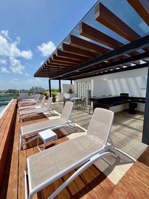 A rooftop lounge with sun loungers, a dining area, and a view of the cityscape. - Studio 5th Av, Fast Wi-Fi, Rooftop Pool & Gym (Playa del Carmen)