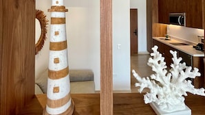 Uma prateleira de madeira com uma maquete de farol, uma escultura de coral branco e uma planta em vaso.