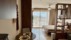 Quarto de hotel com cama, uma mesa de jantar com pratos, máquina de café, estante de livros e vista para o exterior.