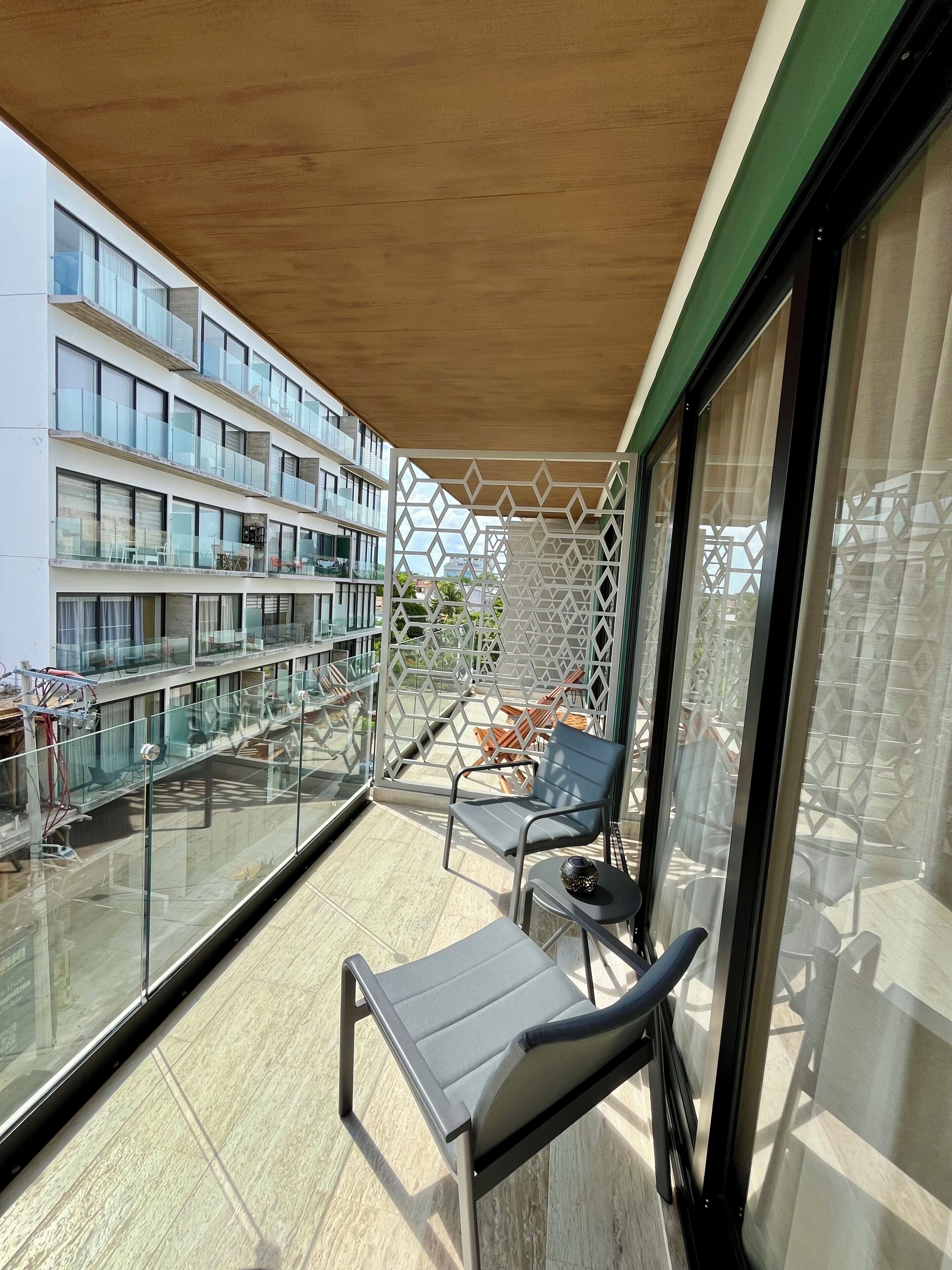 Un balcone con tetto in legno, ringhiere in vetro e vista su un edificio moderno.
