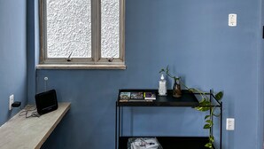 A room with a window, a small table with a plant, and a shelf with books and a bottle. - Modern loft in Belém with solar energy - At Doca Umarizal - downtown (Belém)