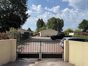 A gated driveway leading to a residential area with houses, a parked black SUV, and a white car.
