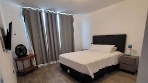 A bedroom with a bed, a nightstand, a TV, and a window with curtains.