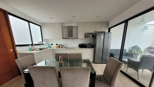 A modern kitchen with a glass dining table, chairs, and a view through large windows.