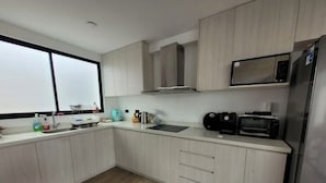 A modern kitchen with light wood cabinets, a stainless steel refrigerator, a microwave, and a toaster.