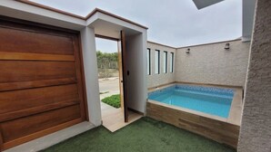 A modern outdoor area with a wooden door, a swimming pool, and a small garden.