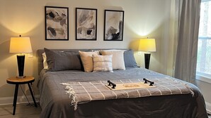 Camera da letto con un letto, due abat-jour, ventola a soffitto e arte astratta alle pareti.