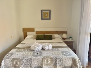 Una cama bien hecha con toallas enrolladas, una mesita de noche con lámpara y un cuadro en la pared.