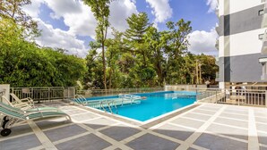 A swimming pool with a tiled deck, surrounded by trees and a building. - 1 Bedroom in Westlands, Nairobi ,parking, WiFi,Gym (Nairobi)