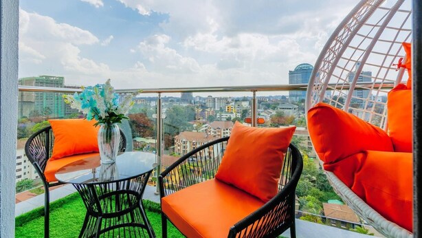 A balcony with wicker chairs and a table, a hanging chair, and a vase with flowers. - 1 Bedroom in Westlands, Nairobi ,parking, WiFi,Gym (Nairobi)