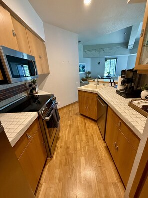 A compact kitchen with wooden cabinets, a microwave, stove, and a dishwasher. - Amazing Mountain Views Palisades Condo A+ Location (Olympic Valley)