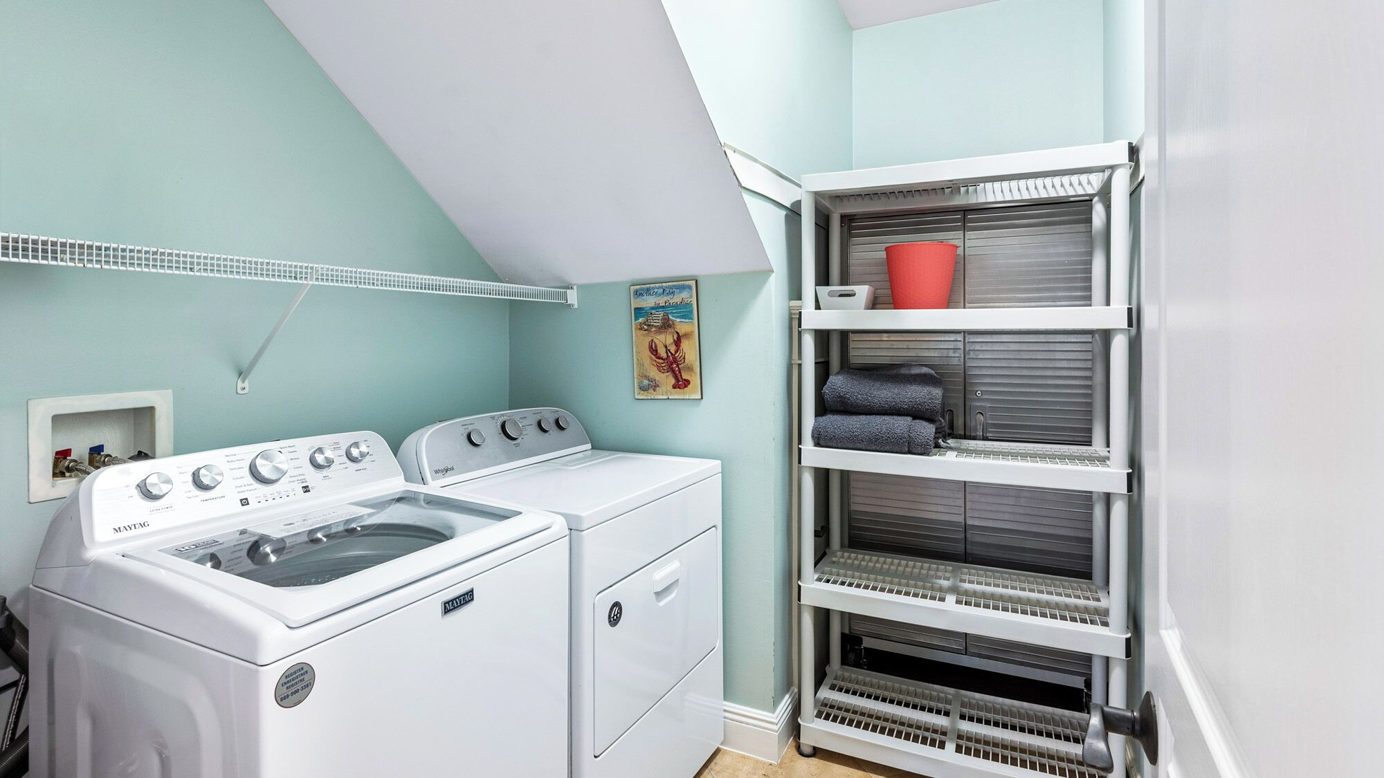 A laundry room with two white washing machines, a drying rack, and a shelving unit with folded towels.