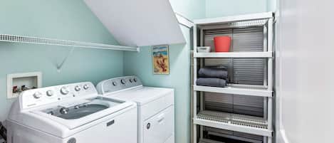 A laundry room with two white washing machines, a drying rack, and a shelving unit with folded towels.
