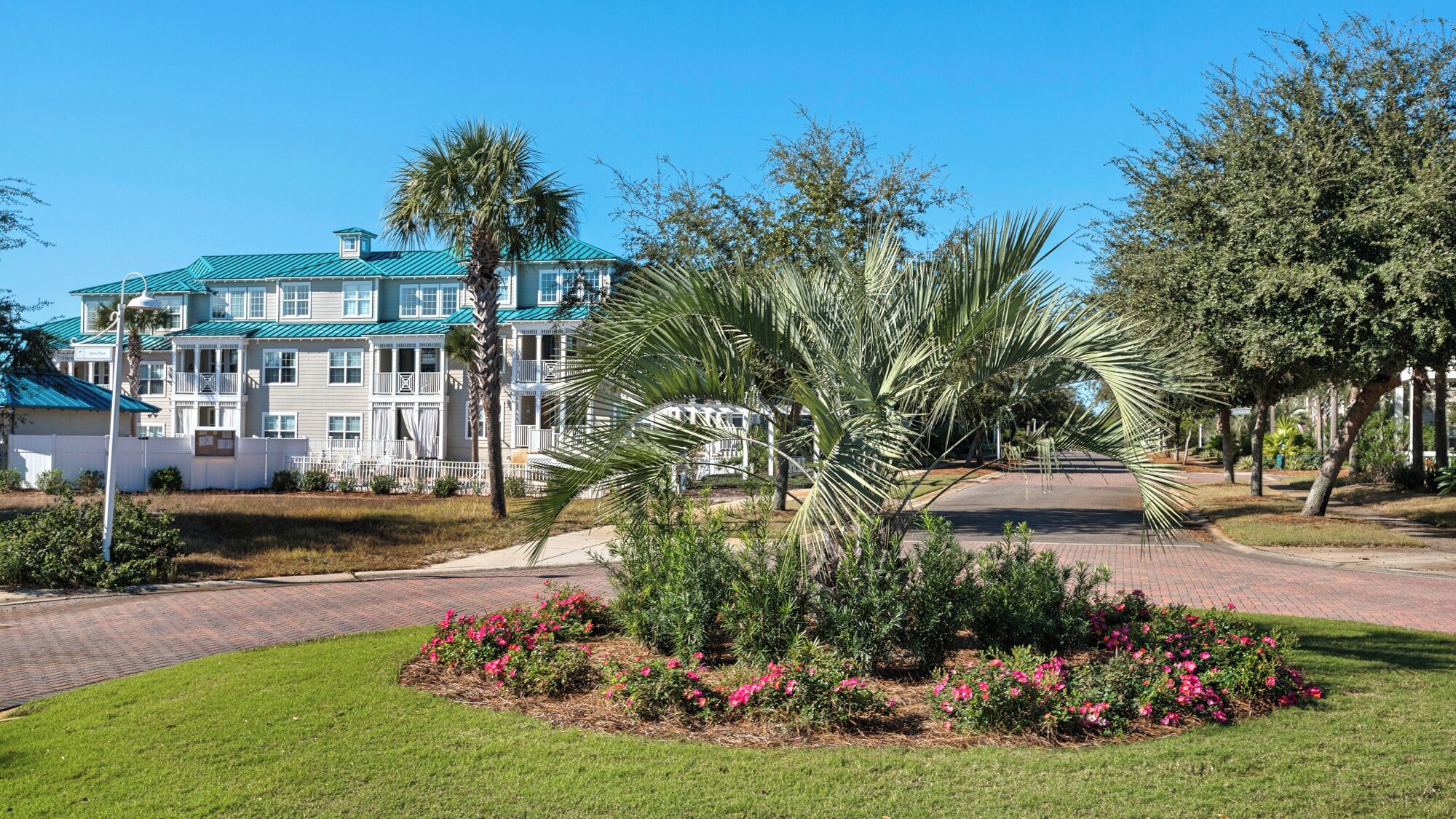 A multi-story hotel with a green roof and white exterior, surrounded by well-maintained lawns and flowering plants.