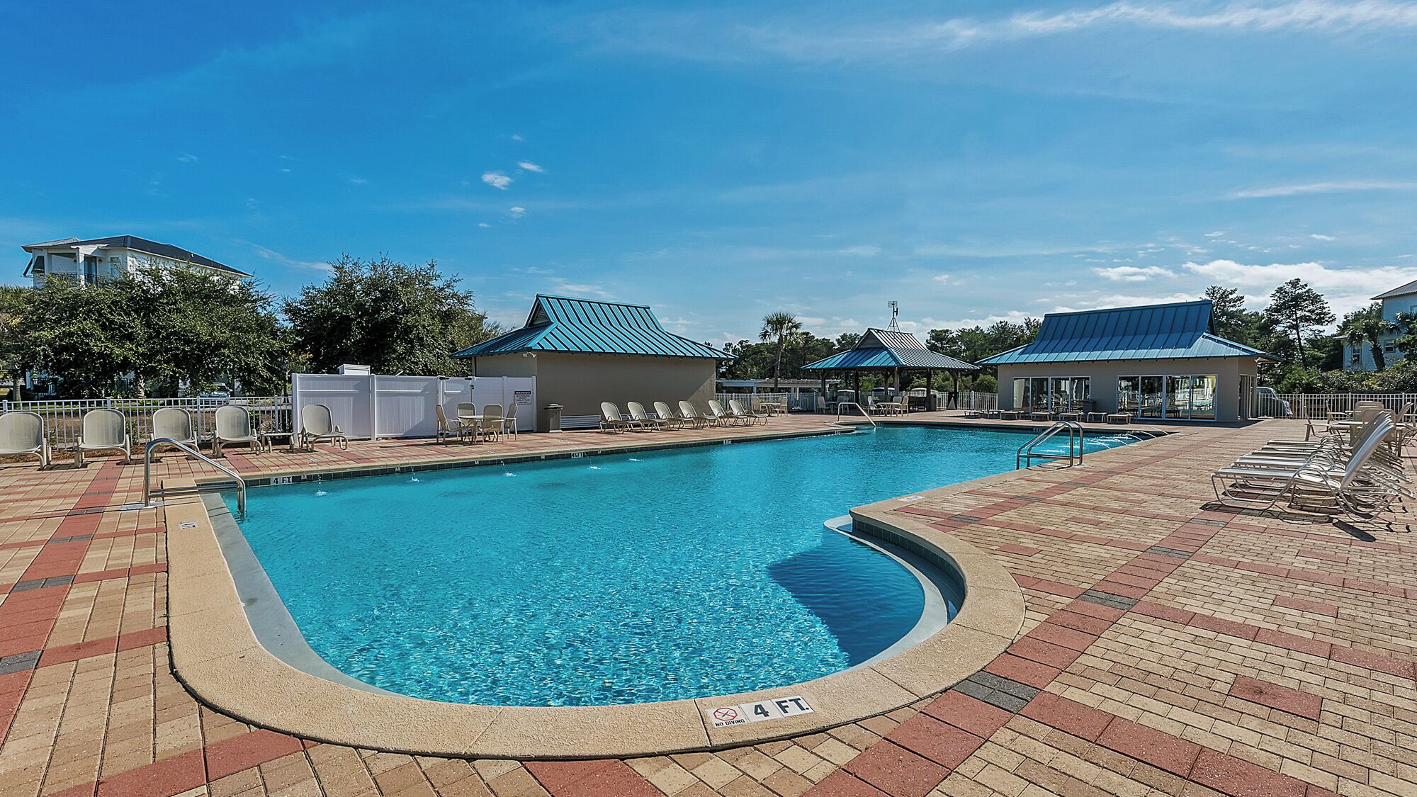 A rectangular swimming pool with a 4 ft. no diving sign, surrounded by lounge chairs and a covered seating area.