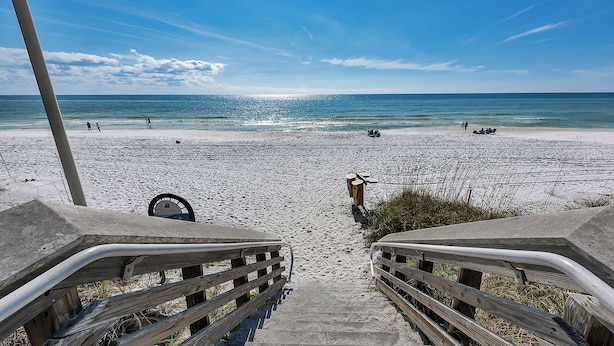 En strand med en træpromenade ned til vandet, et skilt med teksten 'South Walton', og mennesker på stranden.