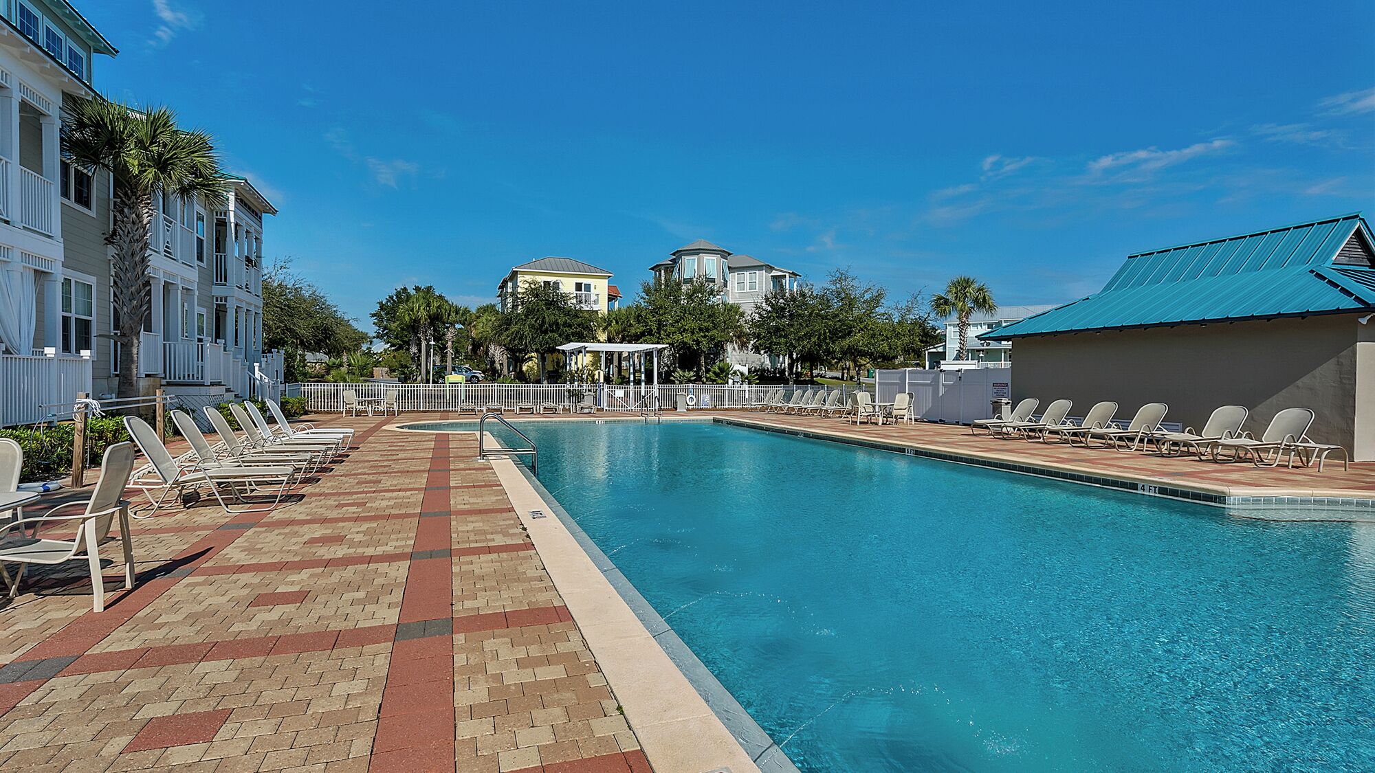 A swimming pool with lounge chairs, a brick walkway, and buildings in the background.