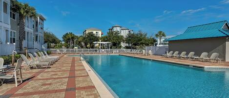 A swimming pool with lounge chairs, a brick walkway, and buildings in the background.