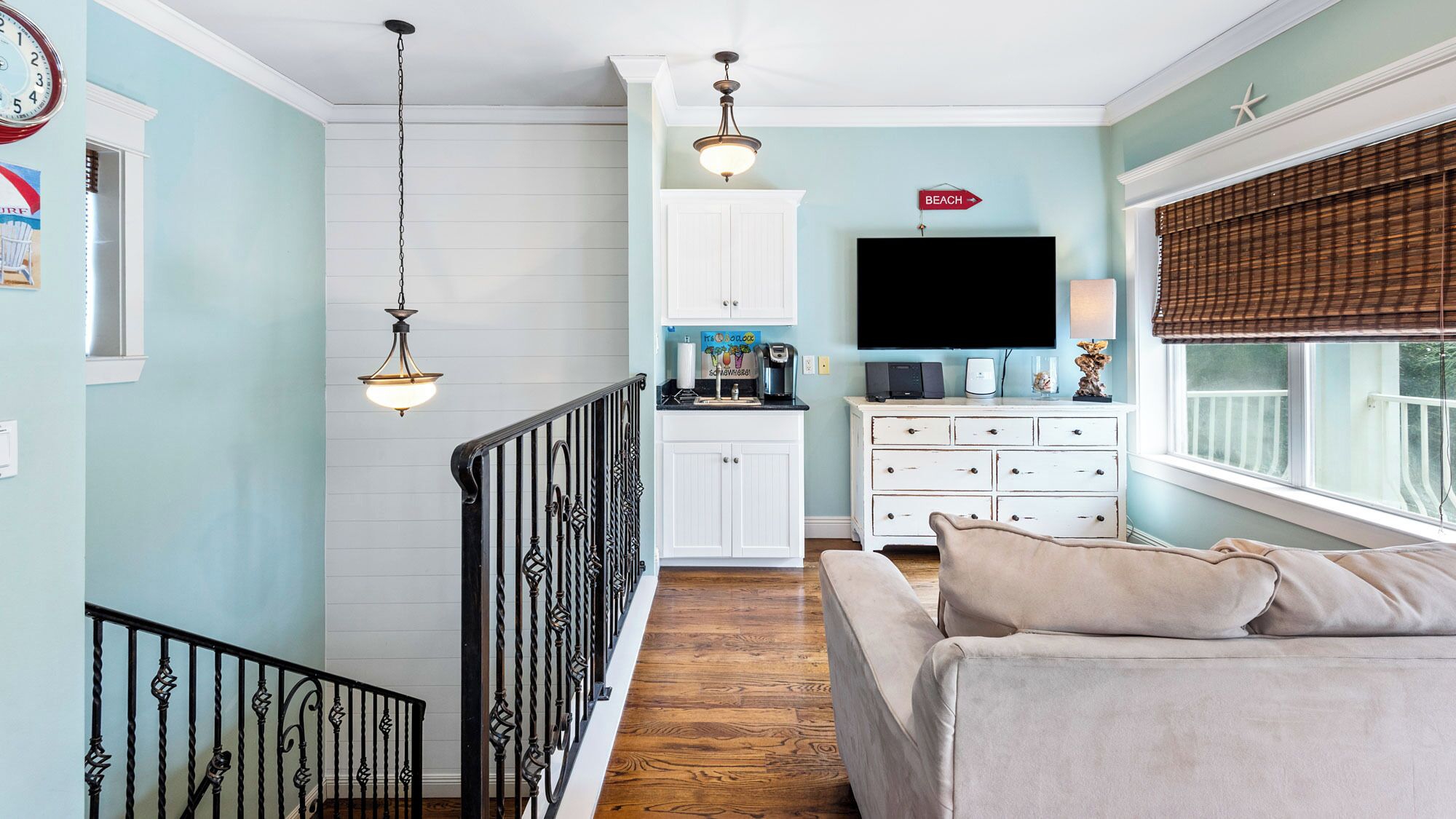 A living room with a sofa, a TV, a kitchen area, and a staircase.