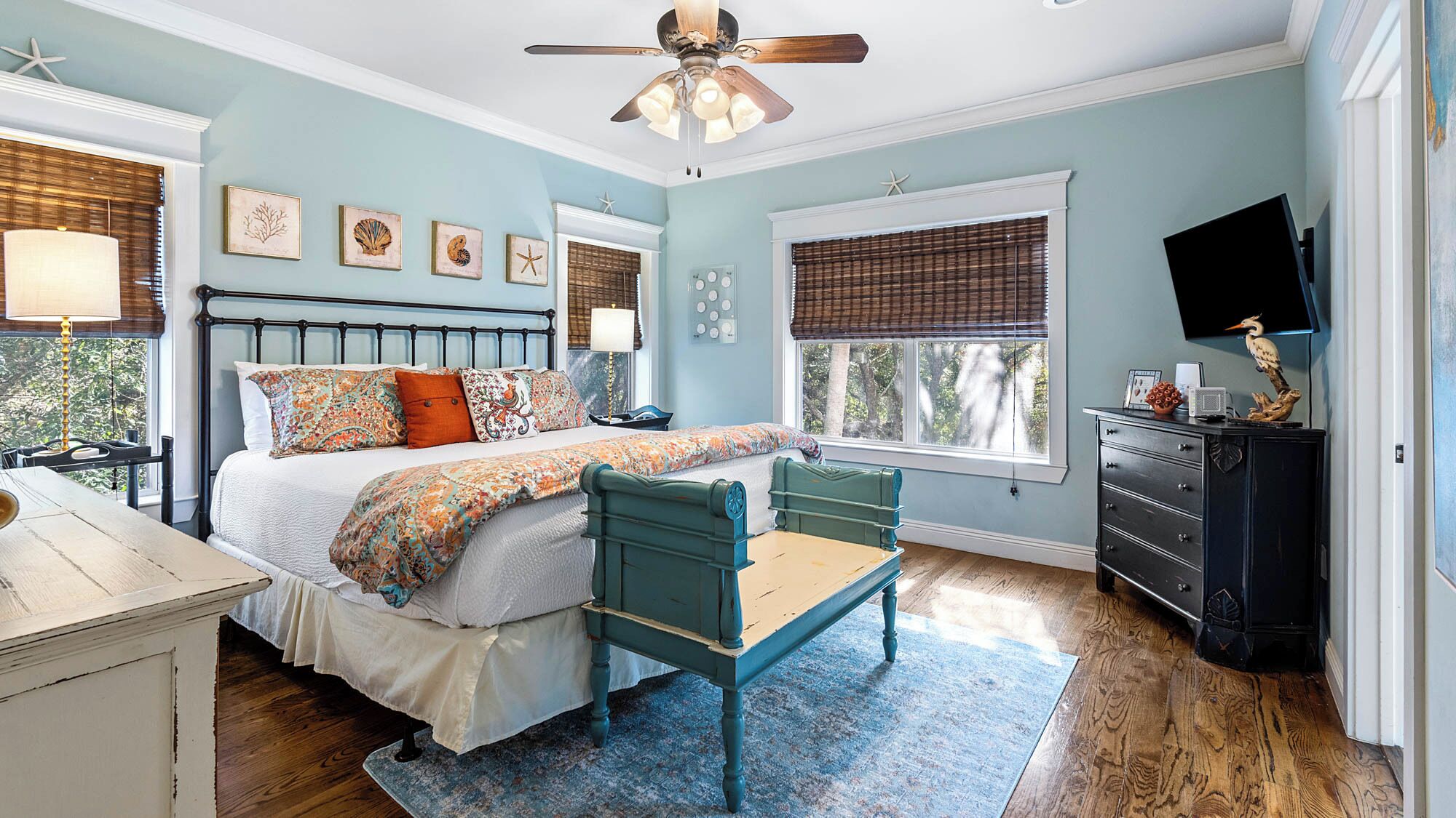 A bedroom with a bed, bedside tables, a desk, a chair, a ceiling fan, and a dresser.