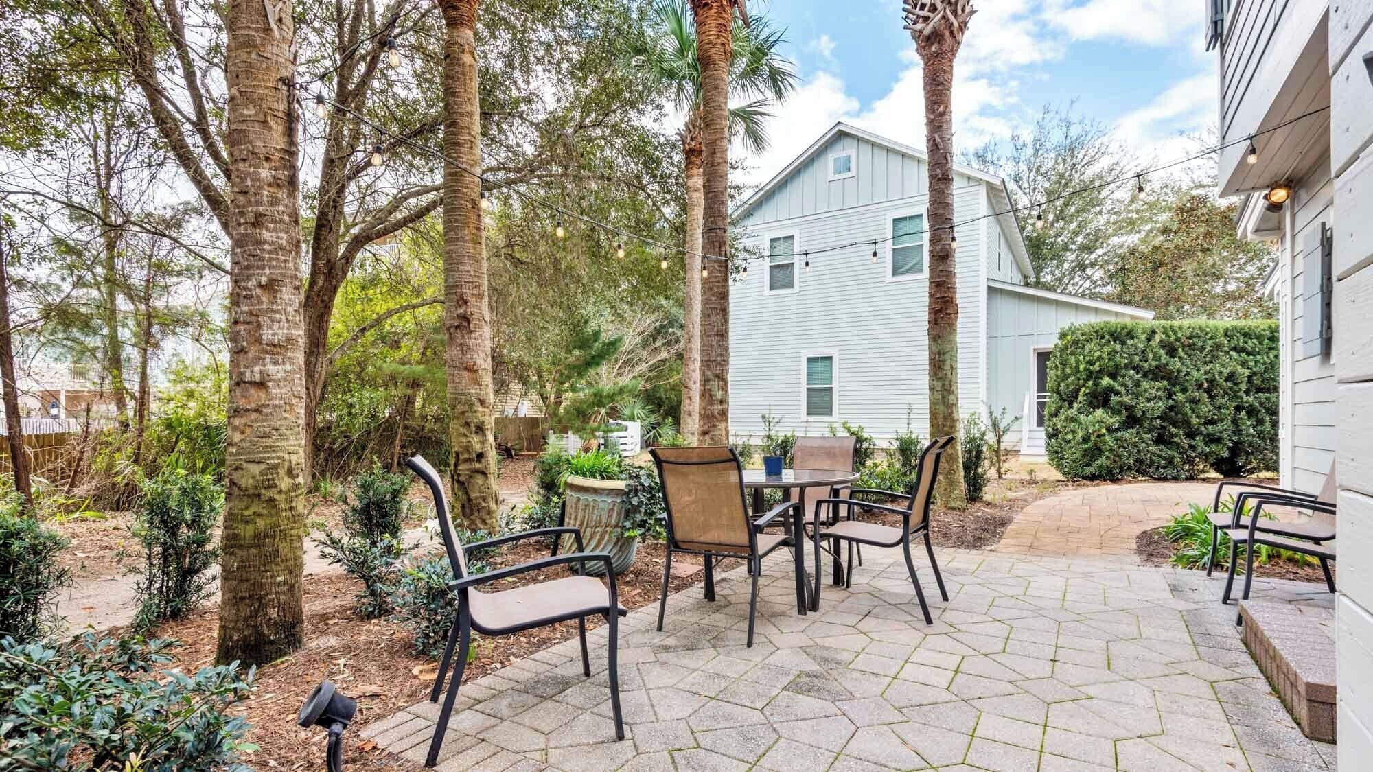Une terrasse avec une table et des chaises, entourée d’arbres et d’une maison.
