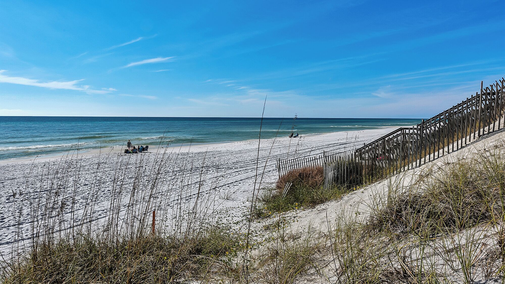 Une plage avec une clôture en bois, des dunes de sable et l’océan.