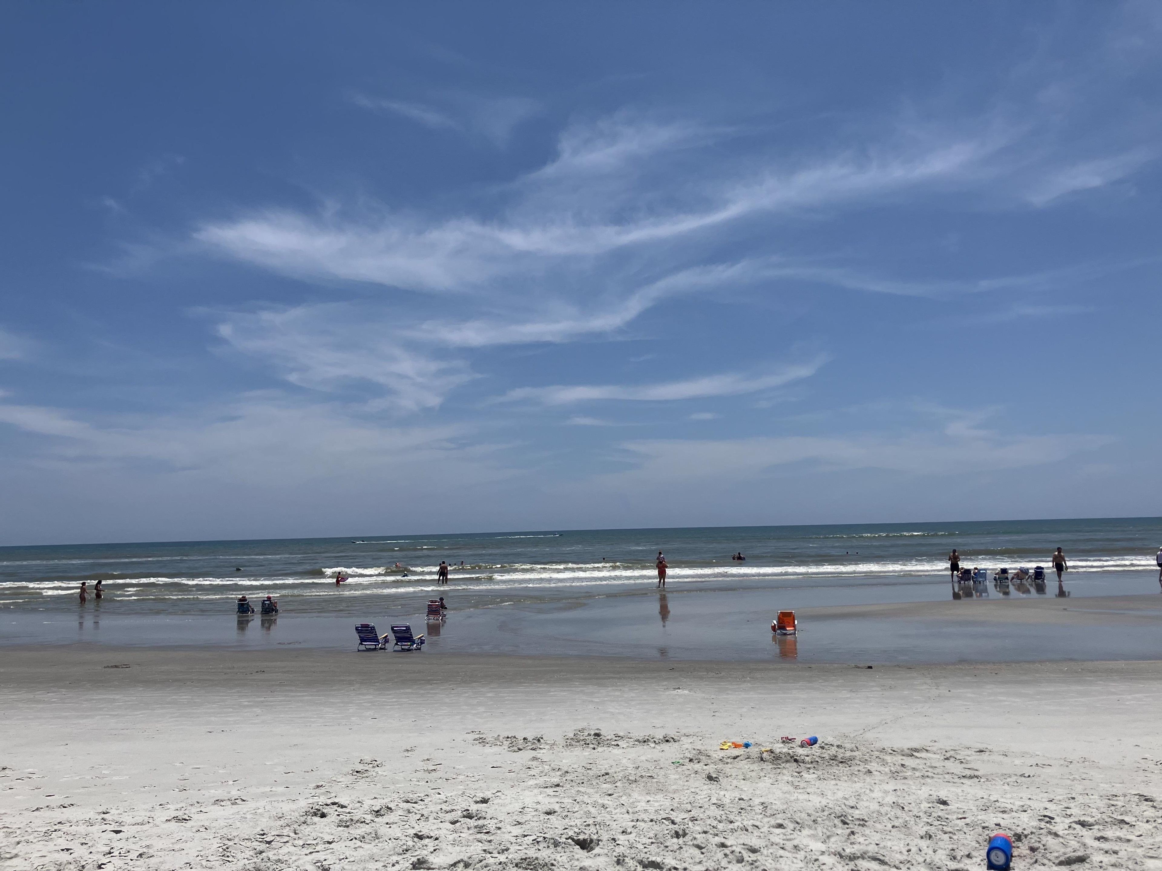 Una platja amb cel blau, aigua tranquil·la i gent gaudint de la riba.