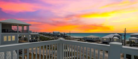 A beachfront property with a balcony overlooking the ocean and a sunset.