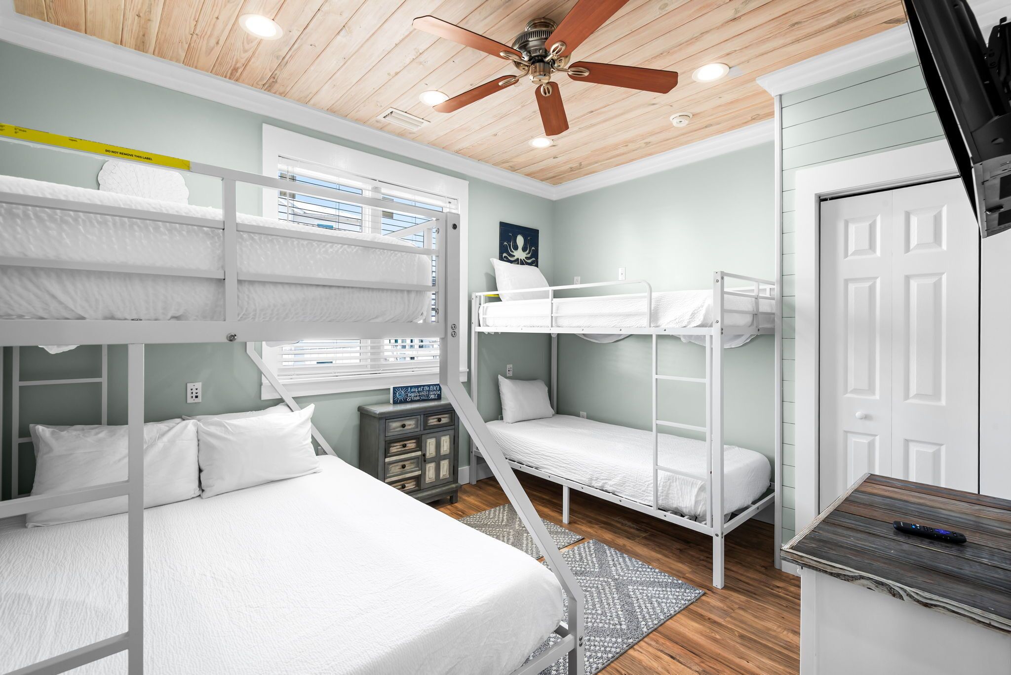 Une chambre avec un lit superposé, un ventilateur de plafond, une fenêtre avec des stores et une porte.