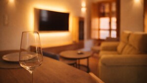 A glass of water on a table in a warmly lit room with a TV mounted on the wall and a sofa in the background.