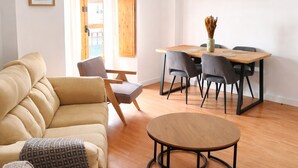 A living room with a sofa, a round coffee table, a dining table with chairs, a ceiling fan, and a wooden door with curtains.