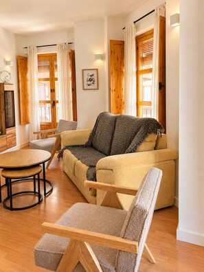 A cozy living room with a sofa, a chair, a small table, and a wooden floor.
