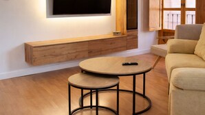 A modern living room with a flat-screen TV mounted on the wall, a wooden bench, a round coffee table, and a sofa.