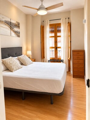 A bedroom with a bed, a ceiling fan, a nightstand, a dresser, and a window with curtains. - ATAIFOR ACCOMMODATIONS IN THE CENTER OF JAÉN (Jaén)