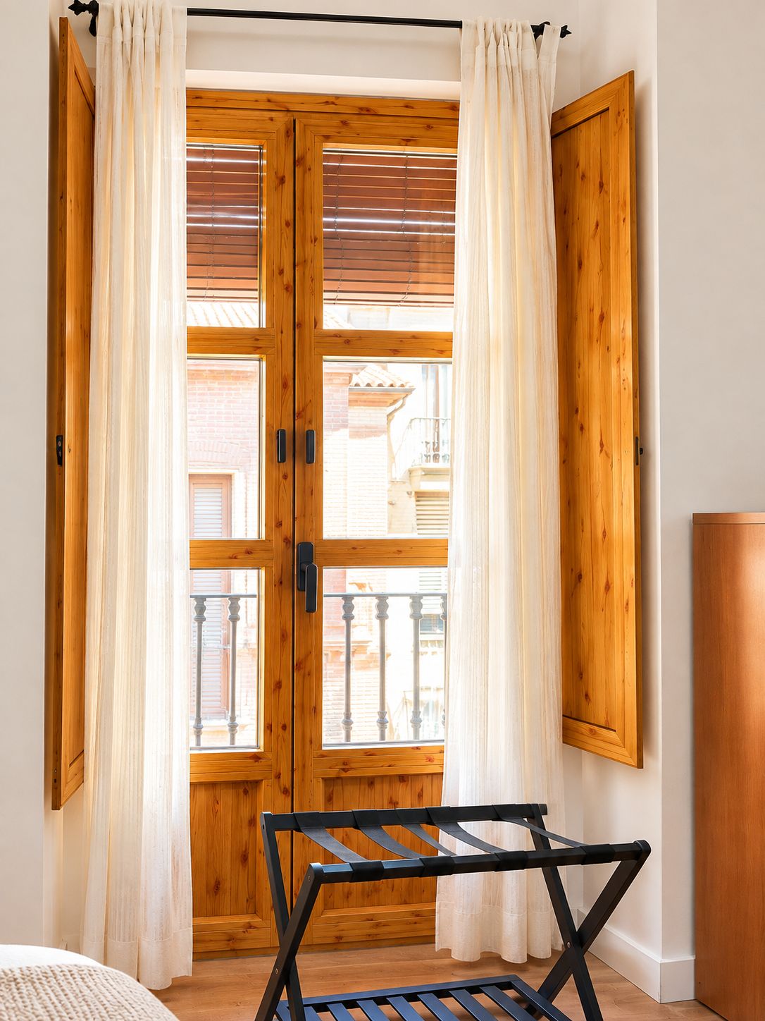 Une pièce avec une porte en bois, des rideaux blancs et une chaise pliante en métal noir.