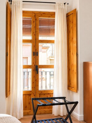 A room with a wooden door, white curtains, and a black metal folding chair. - ATAIFOR ACCOMMODATIONS IN THE CENTER OF JAÉN (Jaén)