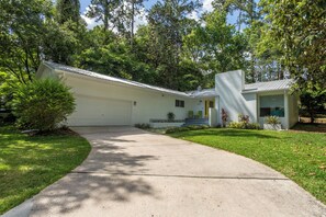 Una casa a piano terra con vialetto che conduce a un garage, circondata da alberi e un prato curato.