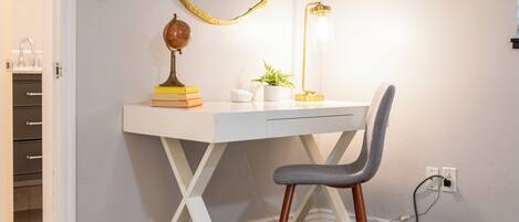 A white desk with a globe, books, and a plant, a gray chair, and a gold-framed mirror on a wall.