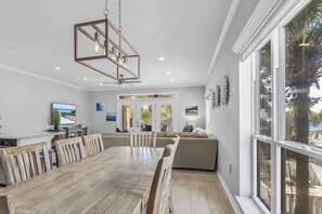 A dining area with a wooden table and chairs, a hanging light fixture, and a view of the outdoors through large windows. - 5BR Home w/ Pool Table in Seagrove - Steps From the Beach & Pool - Sleeps 12 (Santa Rosa Beach)