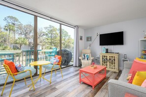 A spacious living area with a balcony, a flat-screen TV, and a comfortable seating arrangement. - Saltwater Pools - Walk to Beach & Coligny Plaza (Hilton Head Island)