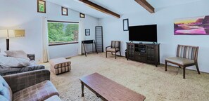 A living room with a sofa, ottoman, TV, and a painting on the wall.