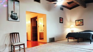 Une chambre à coucher comprenant un lit, une chaise, un ventilateur de plafond, un tableau et une porte donnant sur une autre pièce.