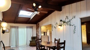Un coin repas avec une table et des chaises, un ventilateur de plafond et une vue sur la cuisine.