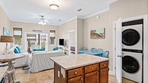 A compact kitchen with a central island, a dining area with blue chairs, and a laundry room with two washing machines.