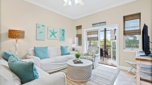 Een woonkamer met een witte bank, turquoise kussens, een ronde salontafel en een schilderij van een zeester. Een bordje geeft de locatie aan als Bradenton, Florida.