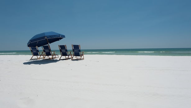 Een strand met drie strandstoelen onder een blauwe parasol, gericht op de zee.