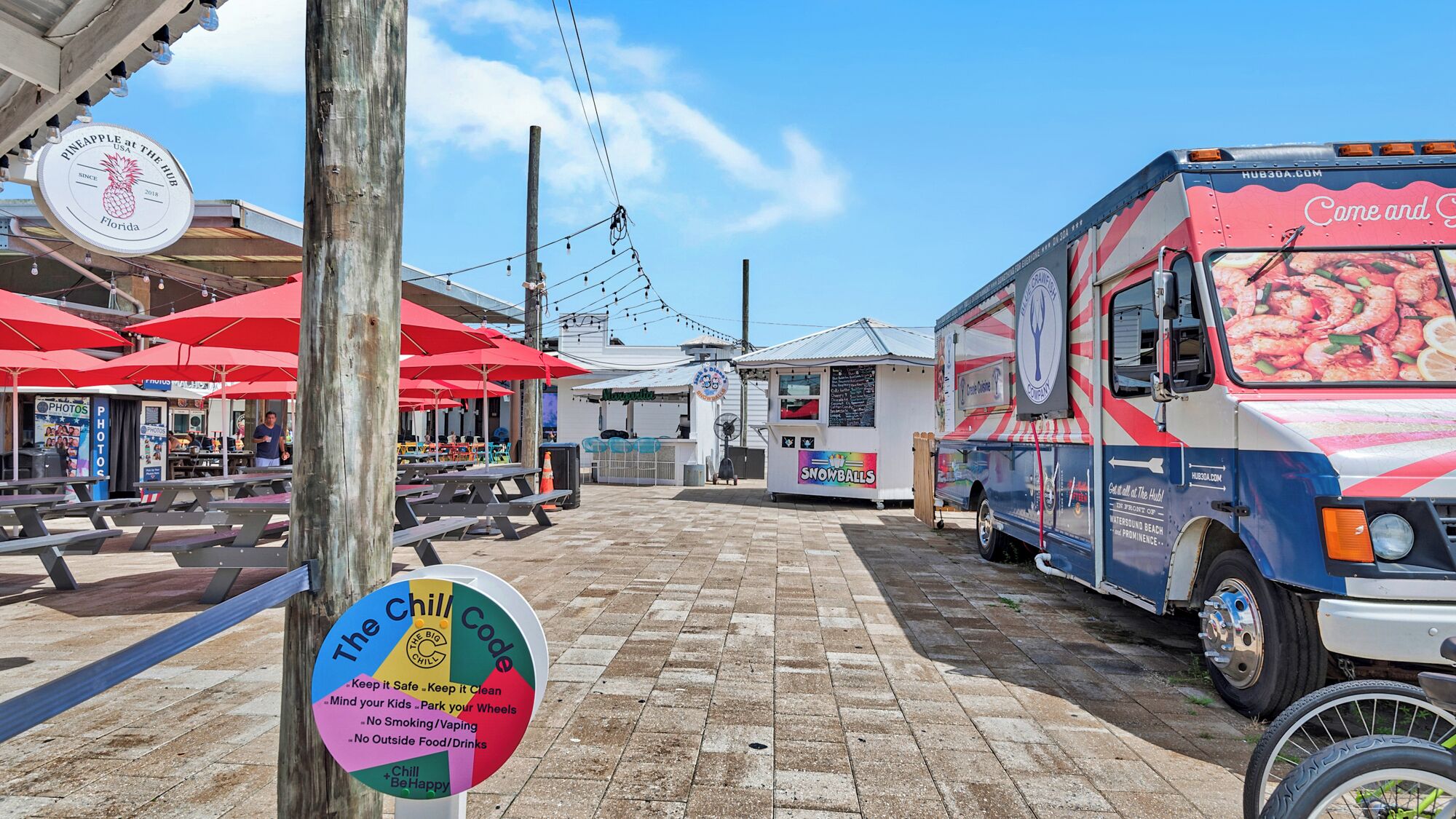 A food truck with a shrimp advertisement parked next to a beachside eatery.