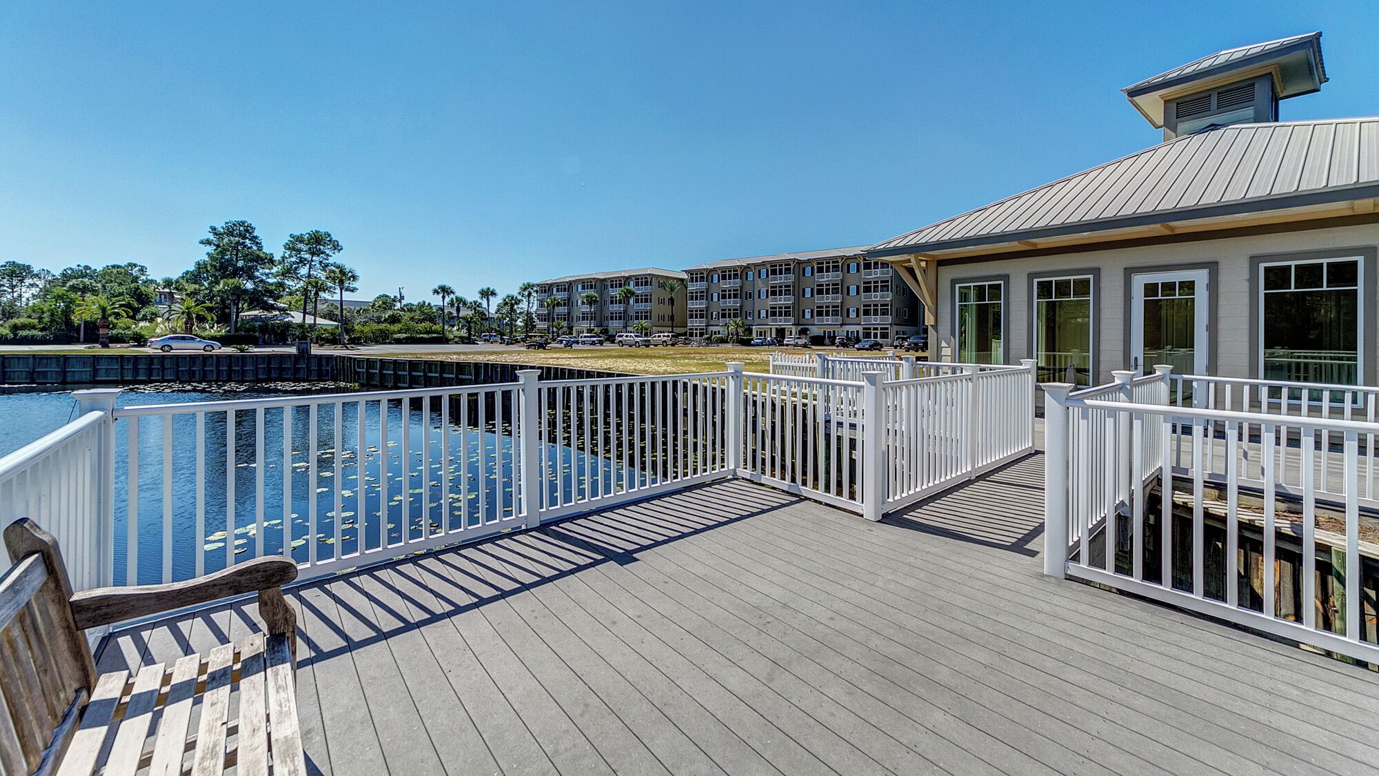 A wooden deck with a pool, white railings, and a view of a multi-story building in the background.